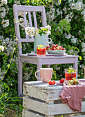 Frische Erdbeeren, Getränke und Blütenstrauß auf Holzstuhl und Holzkiste im Garten