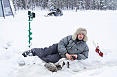 Man lying on ice while fishing from a hole, Lapland, Sweden, Scandinavia, Europe