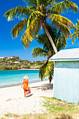 Touristin in orangefarbenem Kleid läuft am palmengesäumten Strand, Antigua, Leeward-Inseln, Westindische Inseln, Karibik, Mittelamerika
