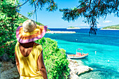 Frau betrachtet das kristallklare Meer unter den Bäumen im Schatten auf einem Hügel, Porto Atheras, Kefalonia, Ionische Inseln, Griechische Inseln, Griechenland, Europa