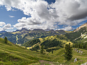 Bergweiden an einem sonnigen Tag mit weißem Wolkenhimmel und Licht, das den Berg darunter beleuchtet, Dolomiten, Italien, Europa