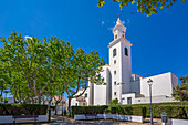 Blick auf die weiß getünchte katholische Kirche, eingerahmt von Bäumen vor blauem Himmel, Sant Lluis, Menorca, Balearen, Spanien, Mittelmeer, Europa