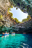 Touristen bewundern die Höhle während einer Bootsfahrt auf dem kristallklaren Wasser des Melissani-Sees, Kefalonia, Ionische Inseln, Griechische Inseln, Griechenland, Europa