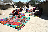 Stammesfrauen legen ihre Stammesstickereien vor den Häusern mit Lehmwänden in ihrem Stammesdorf aus, Kachchh, Gujarat, Indien, Asien