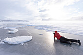Man photographing the snowy landscape lying down on a frozen lake, Stora Sjofallet, Norrbotten County, Lapland, Sweden, Scandinavia, Europe