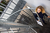 Young female technician carrying ladder on stairs