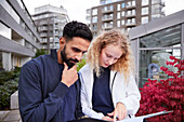 Male and female worker looking at documents in courtyard