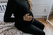 Schwangere Frau auf dem Bett sitzend und Bauch berührend