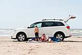Father and sons beside car on beach by sea