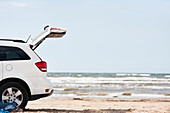Car with open trunk on beach by sea