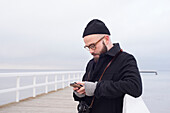 Mann auf Seebrücke mit Smartphone