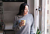 Woman holding mug, looking through window