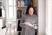 Woman holding note pad, standing by window