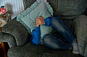Boy sitting in armchair and covering face with cushion