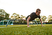 Teenage boy doing push-ups on bench in playing field