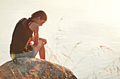 Teenager-Mädchen sitzt auf einem Felsen am See