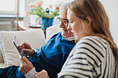 Älterer Mann mit erwachsener Enkelin bei der Nutzung eines digitalen Tablets