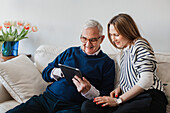 Senior man with adult granddaughter using digital tablet