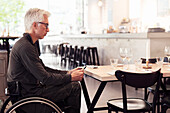 Man on wheel chair, using smartphone in restaurant