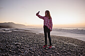 Girl on beach at sunset taking photos