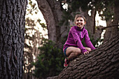 Mädchen kniend auf einem Baumstamm