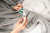 Mann mit Thermometer und Tabletten im Bett