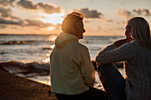 Paar sitzt bei Sonnenuntergang am Strand