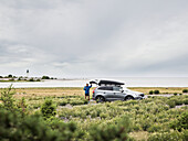 Man standing next to car at seaside