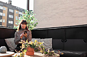 Frau sitzt auf der Terrasse und benutzt ein Mobiltelefon