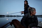 Frau sitzt in einem Boot, während ein Teenager im Hintergrund angelt