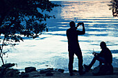 Silhouette of two men by lake at dusk