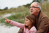 Grandfather sitting with granddaughter on beach