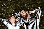 Father and son wearing similar stripped shirts lying on grass