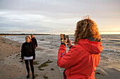 Frau fotografiert Freunde am Strand mit ihrem Smartphone