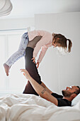 Father playing with daughter in bed