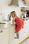 Mädchen klettert auf Schrank in Küche