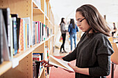 Teenage girl reading book near bookshelf