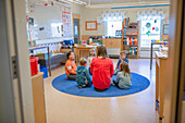 Lehrerin sitzt mit Kindern auf dem Boden