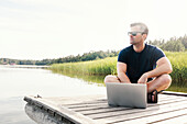 Mann mit Laptop auf dem Bootssteg