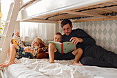 Vater mit Söhnen, die auf dem Bett ein Buch lesen