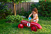 Toddler girl pouring water over ride-on car