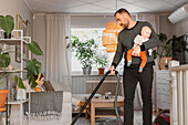 Father carrying baby while vacuum cleaning