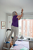 Ältere Frau hängt Deckenlampe auf