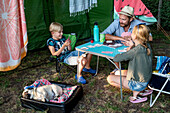 Vater mit Kindern beim Kartenspielen vor dem Zelt