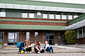Kinder sitzen vor dem Schulgebäude