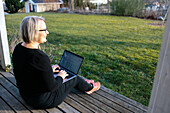 Woman sitting on porch and working on laptop