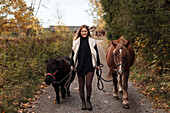 Woman walking with horses on country road