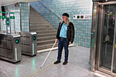 Man with white cane standing at metro station