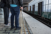 Mann mit weißem Stock am Bahnhof stehend