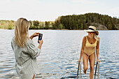 Woman photographing friend while bathing in lake